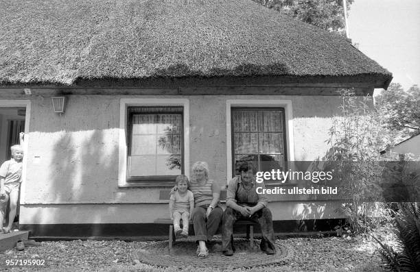 Eine junge Familie sitzt auf einer Bank vor einem Haus in dem kleinen Fischerdörfchen Vitt auf der Insel Rügen, aufgenommen im Sommer 1988. Der Mann...