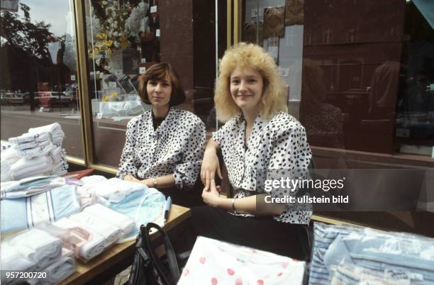 Zwei Verkäuferinnen bieten in der Brunnenstraße in Berlin-Ost Textil-Produkte auf dem Gehweg vor dem Geschäft an, undatiertes Foto von 1990. Mit der...