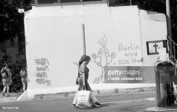 Zwei Frauen laufen mit Tüten an den Resten der Berliner Mauer am ehemaligen Grenzübergang Heinrich-Heine-Strasse in Ostberlin vorbei, aufgenommen im...