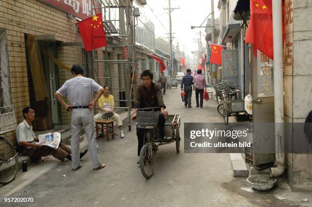 Oktober 2009 / China - Peking / Straßenszene und Alltag, ein Mann liest vor einem Geschäft in einer Zeitung, in einer der benachbarten Straßen und...