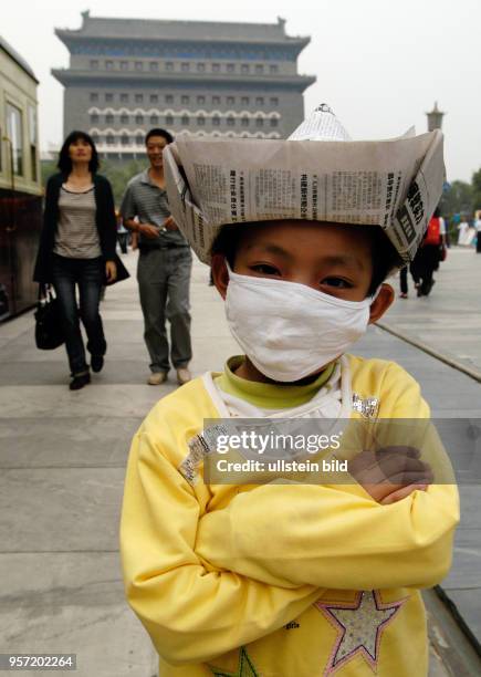 Oktober 2009 / China - Peking/ Ein kleiner chinesischer Junge mit Mundschutz und einem aus einer Zeitung gefalteten Hut auf dem Kopf posiert in der...