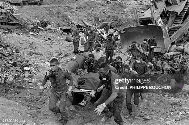 French paratroopers carry the body of a dead soldier, as they continue searching for survivors, 26 October 1983 in Beirut, through the rubble of the...