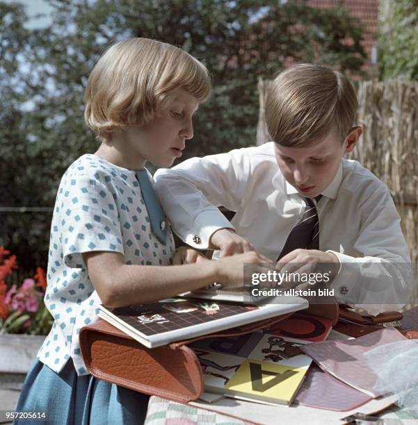 Ein Mädchen und ein Junge schauen sich die Bücher aus ihren Schultaschen bei der Einschulung an, undatiertes Foto von 1963.