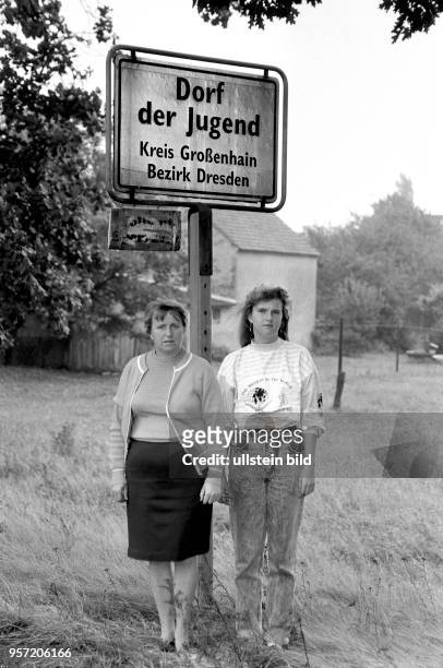 Im August 1990 stehen die Bürgermeisterin Hannelore Gesell und ihre Tochter Anja am Ortsschild des "Dorfes der Jugend" im Kreis Großenhain im Bezirk...