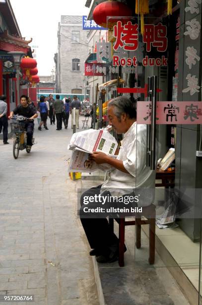 Oktober 2009 / China - Peking / Straßenszene und Alltag, ein Mann liest vor einem Geschäft in einer Zeitung, in einer der benachbarten Straßen und...