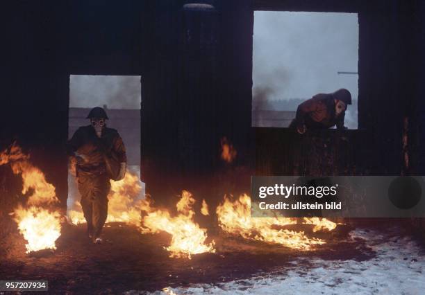 Infanteristen der Nationalen Volksarmee durchlaufen mit aufgesetzten Gasmasken im winterlichen Gelände bei einer Übung ein Hindernis aus Feuer,...