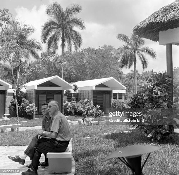 Zwei Männer sitzen auf einer Bank in einer Ferienanlage im Ort Saroa in der Provinz Pinar del Rio , aufgenommen 1962.