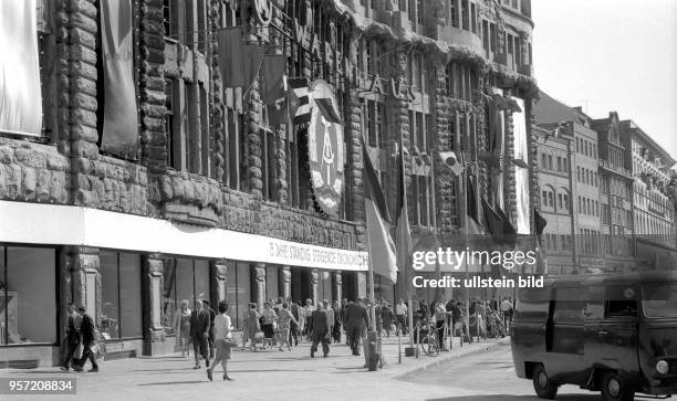 Fahnen und das Staatswappen der DDR zieren die Außenfassade des Konsum-Warenhauses am Brühl in der nördlichen Leipziger Altstadt, aufgenommen 1964.