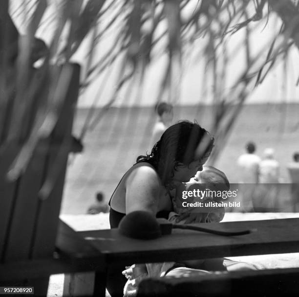 Eine junge Mutter mit ihren Kindern am Strand von Santa Maria del Mar bei Havanna unter einer Palme, , aufgenommen 1962.