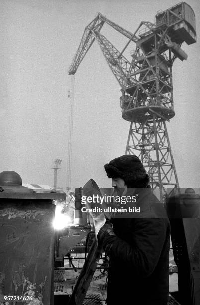 Ein Arbeiter mit Pelzmütze und dicker Bekleidung beim Elektro-Schweißen an einer Stahlkonstruktion im VEB Kranbau Eberswalde, aufgenommen 1987.