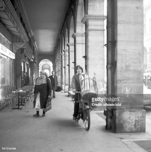Ein Jugendlicher in einer Einkaufsstraße in Paris transportiert auf seinem Moped einen Korb Baguettebrote, aufgenommen im November 1970.