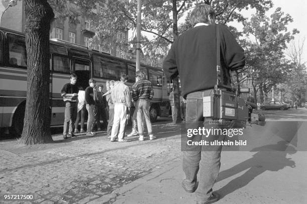 Ein Kameramann mit umgehängter Kamera mit ZDF-Logo läuft auf eine Gruppe von DDR-Flüchtliongen zu, die an einem Bus in Warschau auf ihre Ausreise...