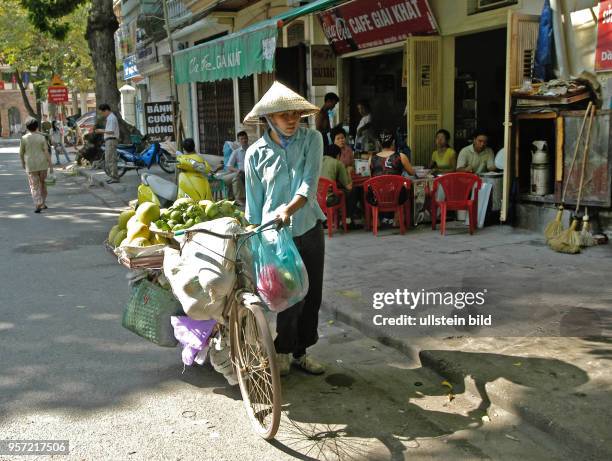 Eine Frau schiebt ein mit Einkäufen voll beladenes Fahrrad in der Altstadt von Hanoi, der Hauptstadt der Sozialistischen Republik Vietnam,...