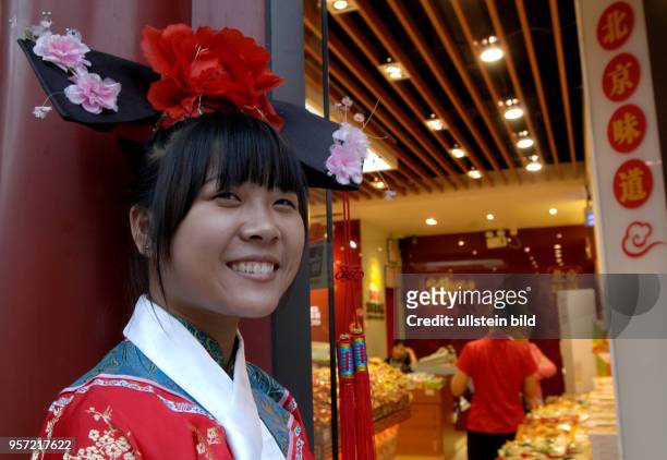 Oktober 2009 / China - Peking/ Passanten und Touristen -Eine Verkäuferin in traditioneller Kleidung vor einem Geschäft in der sanierten alten...