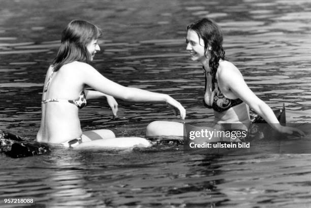 Zwei Frauen in gemusterten Bikinis sitzen auf einer Luftmatratze im Wasser in Berlin Schmöckwitz, aufgenommen 1976.
