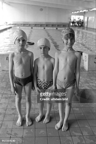 Drei Kinder in Badebekleidung in sicherer Entfernung zum Wasser, aufgenommen im Mai 1982 in der Schwimmhalle der Lutherstadt Eisleben .