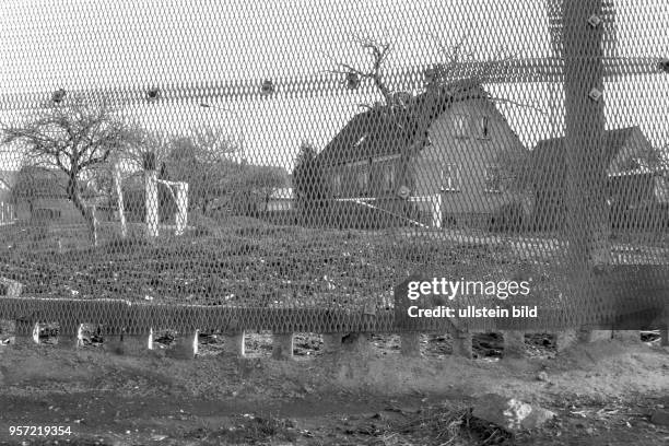 Graue Häuser, Garten und eine Schranke hinter dem Metallgitterzaun der innerdeutschen Grenze im DDR-Dorf Göddeckenrode zwischen Sachsen-Anhalt und...