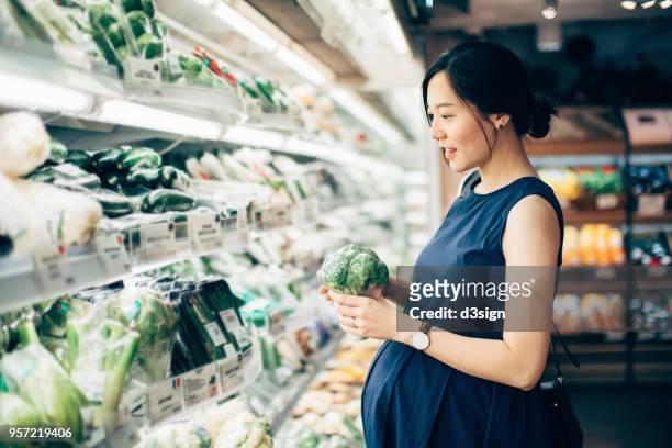 Asian pregnant woman grocery shopping at the vegetable aisle in supermarket