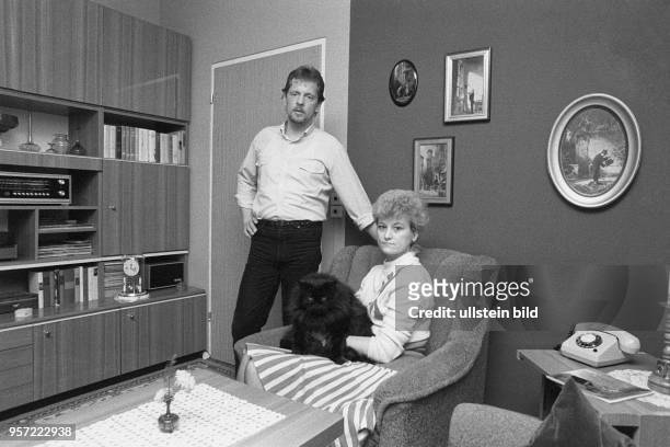 Ein Ehepaar mit einer Rassekatze posiert in ihrem Wohnzimmer mit Schrankwand und Telefon, aufgenommen 1986 in einer Neubauwohnung in einem Plattenbau...