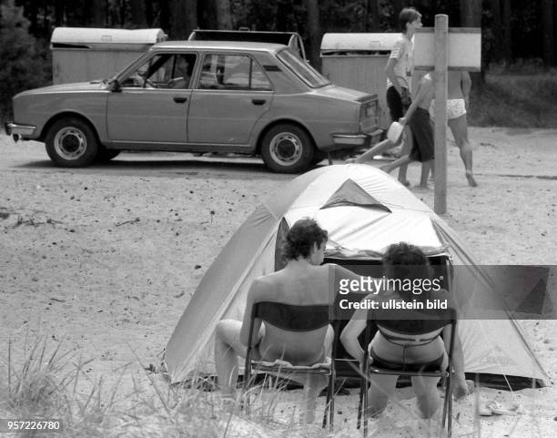 Ein junges Paar in Badebekleidung sitzt vor seinem Zelt auf dem Campingplatz im Ostseebad Prerow auf dem Darß, aufgenommen im Sommer 1990. Der...