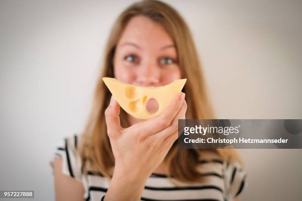 woman holding cheese in front of her face - swiss cheese foto e immagini stock