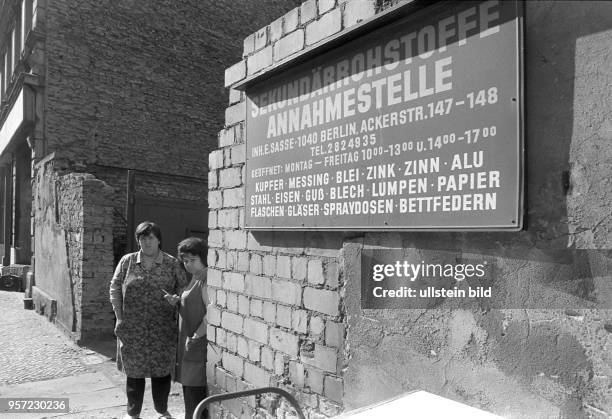 Zwei Frauen in Kittelschürzen stehen an der unverputzen Eingangsmauer zum einem Hof in der Ackerstraße 147-148, auf dem eine...