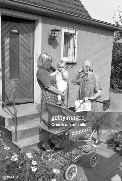 Eine junge Frau mit Kind und eine alte Frau mit einer Tageszeitung in der Hand stehen vor einem kleinen Einfamilienhaus in Magdeborn bei Leipzig,...