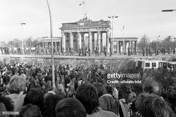 Menschenmassen stehen im November 1989 auf der West-Seite der Berliner Mauer am Brandenburger Tor. Soldaten der DDR-Grenztruppen sorgen dafür, dass...