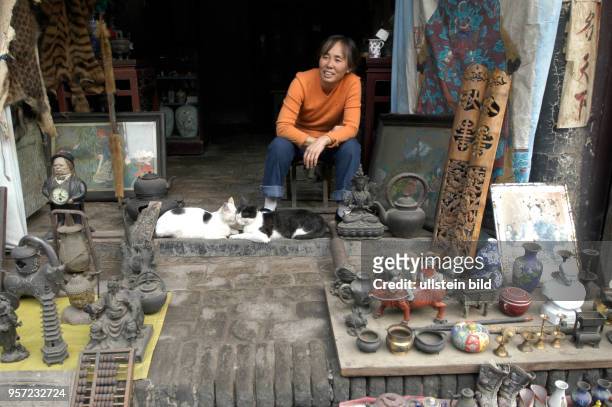 Auf dem Flohmarkt in Pingyao offeriert eine Frau unter anderem Plastiken, Gemälde und diverse Gefäße, aufgenommen am . Neben ihr spielen zwei Katzen....