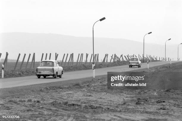 Zwei Pkw vom Typ Trabant fahren an einer Reihe von Betonpfählen vorbei, die hier bei Lüttgenrode an der innerdeutschen Grenze zwischen Sachsen-Anhalt...