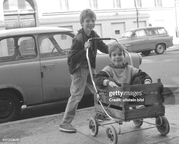 Mit einem umgebauten Kinderwagen sind diese Jungen im Ost-Berliner Stadtbezirk Prenzlauer-Berg unterwegs, am Straßenrand steht ein Trabant,...