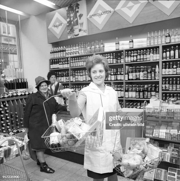 Eine Verkäuferin hält einen Einkaufskorb in einem Geschäft vor Regalen mit Wein und Spirituosen in Eisenach, undatiertes Foto aus dem Jahr 1974.