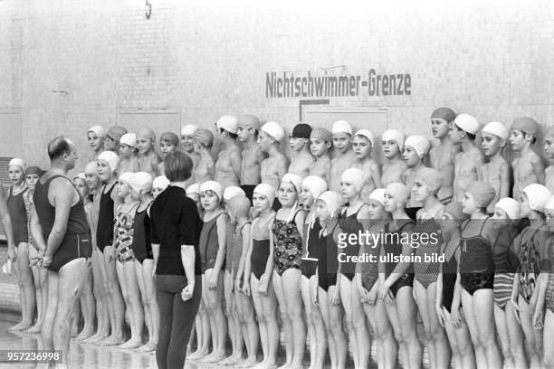 In einer Schwimmhalle in Berlin sind Jungen und Mädchen in Badekleidung und mit Badekappen zum Schwimmunterricht angetreten - Bademeister und...