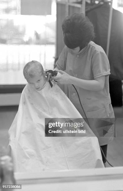 Eine Friseuse schneidet einem kleinen Jungen im Salon "Figaro" in Karl-Marx-Stadt die Haare, aufgenommen im Dezember 1966.