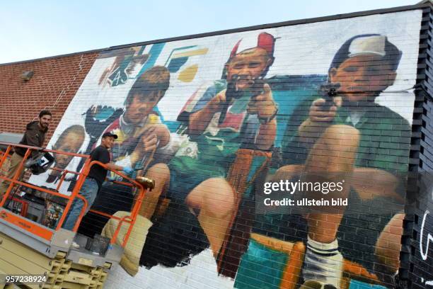 Auf einem Hubwagen stehen zwei Künstler und bemalen eine Ziegelwand an einem Gebäude in Williamsburg, einem heute hippen Stadtteil von Brooklyn.