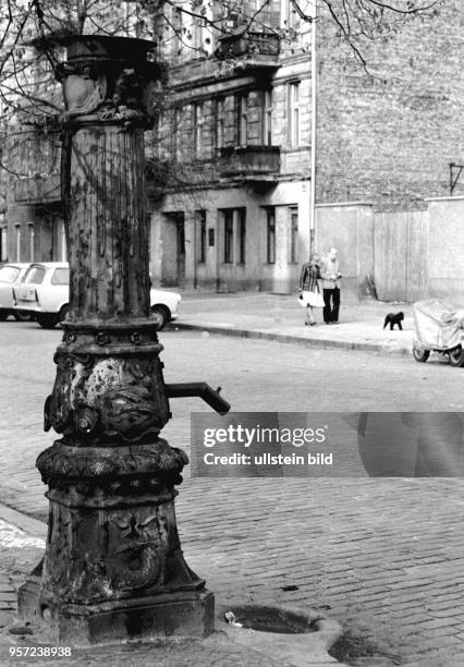 Diese alte Wasserpumpe steht am Straßenrand im Berliner Bezirk Prenzlauer Berg, aufgenommen um 1980 im Frühjahr. Im Hintergrund führt ein Paar ihren...