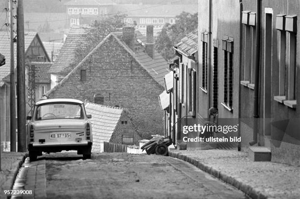 Ein Kind beim Anziehen der Schuhe vor dem Wohnhaus, aufgenommen im Juni 1983 in Hettstedt . Am Straßenrand parkt ein Pkw der Marke Trabant.