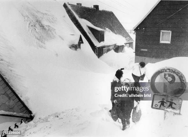 Drei Frauen kämpfen sich durch tiefen Schnee im osterzgebirgischen Altenberg, aufgenommen in den 1970er Jahren. Selbst die Häuser sind komplett...