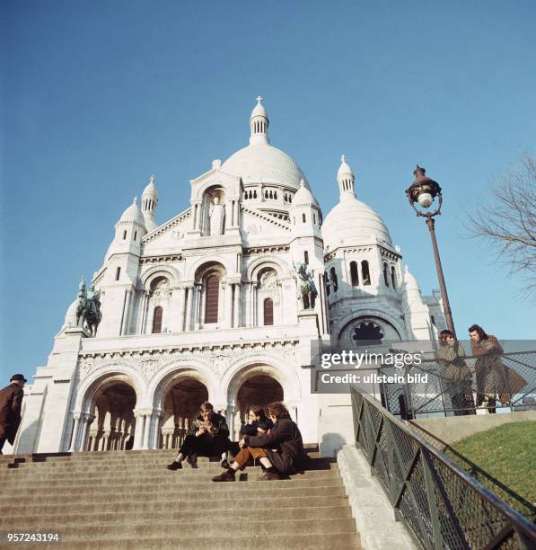 Junge Leute sitzen auf einer Treppe vor der Basilika Sacre Coeur de Montmartre, aufgenommen im November 1970 in Paris. Die Basilika steht auf dem...
