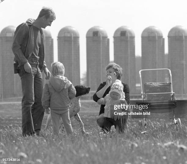 Eine junge Familien mit zwei Kindern und Hund auf einer Wiese vor Silos eines Landwirtschaftsbetriebes in der Gemeinde Frießnitz bei Gera,...