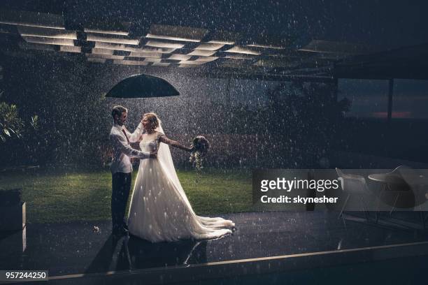 full length of happy newlyweds under the umbrella during rain. - wedding umbrella stock pictures, royalty-free photos & images