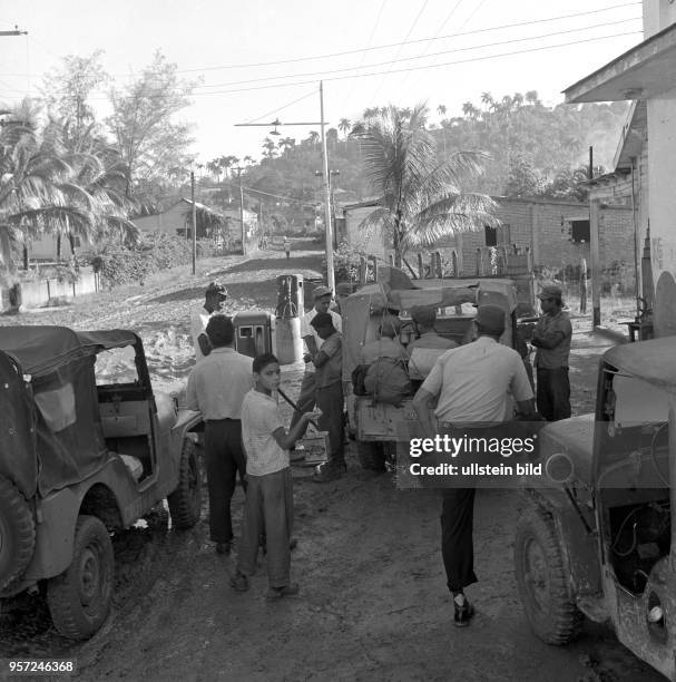 Menschen und Fahrzeuge warten an einer Tankstelle an einer Straße in einem Dorf in der Gebirgsregion Sierra Maestra , aufgenommen 1962.