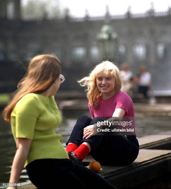 Zwei Besucherinnen sitzen im Hof des Zwingers in Dresden an einem Brunnenrand und genießen die ersten Sonnenstrahlen, aufgenommen im Frühjahr 1988.