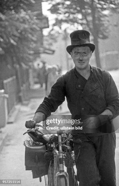 Ein Schornsteinfeger schiebt sein Fahrrad auf dem Gehsteig in der Klement-Gottwald-Allee im Stadtbezirk Weißensee in Berlin , aufgenommen im Sommer...