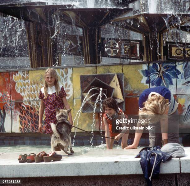 Kinder stehen im Wasser im "Brunnen der Völkerfreundschaft" auf dem Alex in Berlin und bespritzen einen am Rand stehenden Hund, aufgenommen am . Im...
