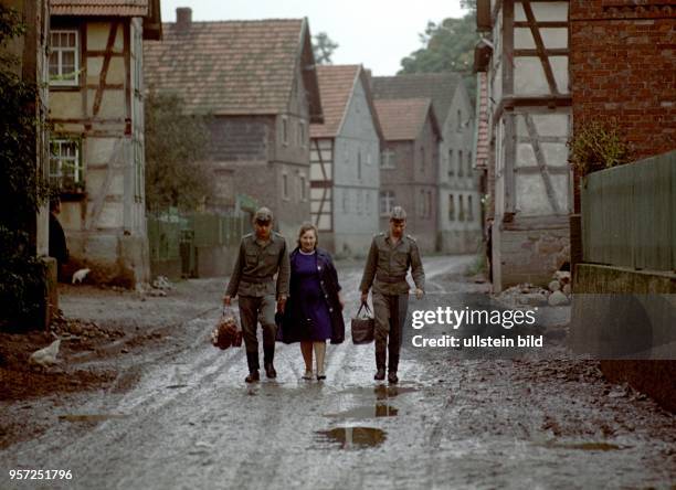 Zwei Grenzsoldaten der DDR-Grenztruppen der Nationalen Volksarmee der DDR tragen der Köchin Berta Niebel der Grenzeinheit Taschen und Einkaufsnetze...