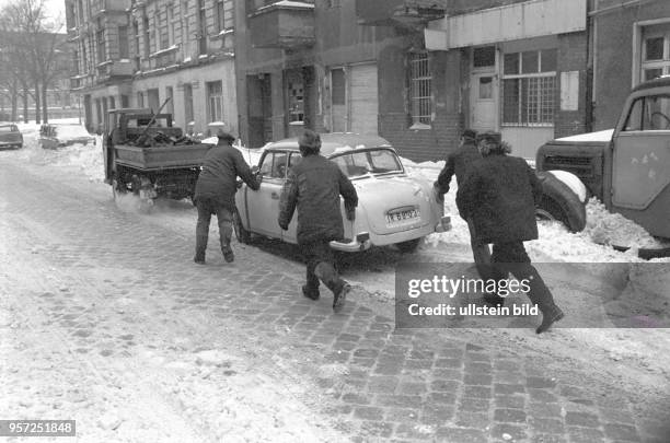 Ein wegen der Kälte mit Startschwierigkeiten liegen gebliebener Trabant wird von einem kleinen Transportfahrzeug angeschleppt und Männer schieben...