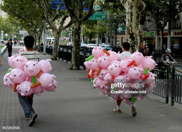 Oktober 2009 / China - Shanghai / Händler tragen Trauben bunter Ballons in Form kleiner Schweinchen auf einer Nebenstraße und gehen zur Fußgängerzone...