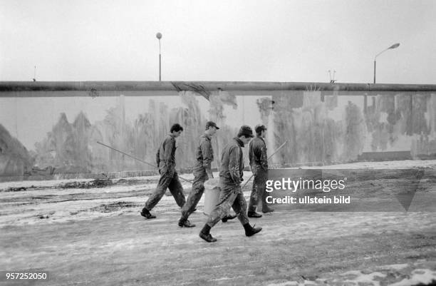 Grenzer tragen Farbroller und einen Farbeimer und haben Bilder und Schriftzüge an der Berliner Mauer am Potsdamer Platz mit weißer Farbe übermalt,...
