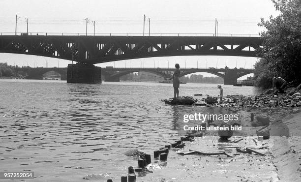 Kinder angeln und planschen am Ufer der Weichsel, mit zwei Brücken im Hintergrund, aufgenommen 1975 in Polen.